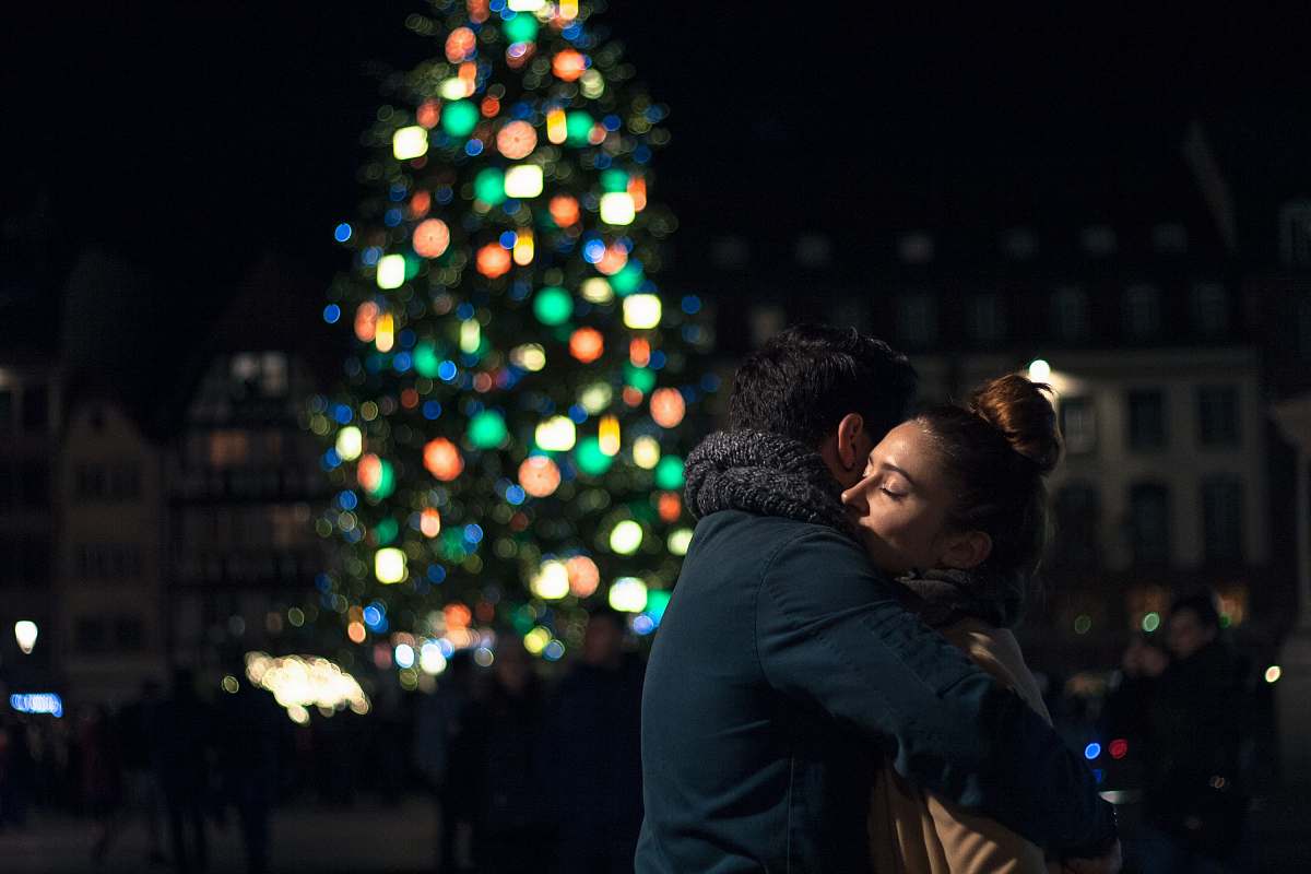plant selective focus photography of man and woman hugging each other near Christmas tree tree
